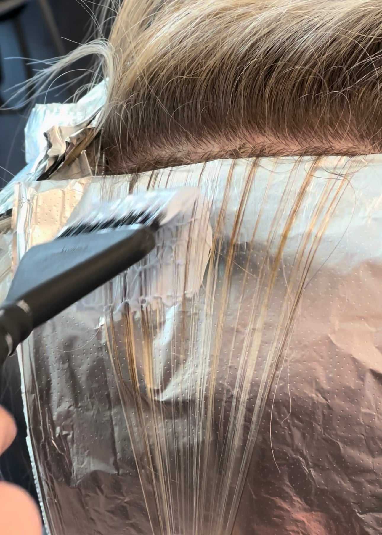 Hair being highlighted with a brush and foil. Close-up of application process at a salon.