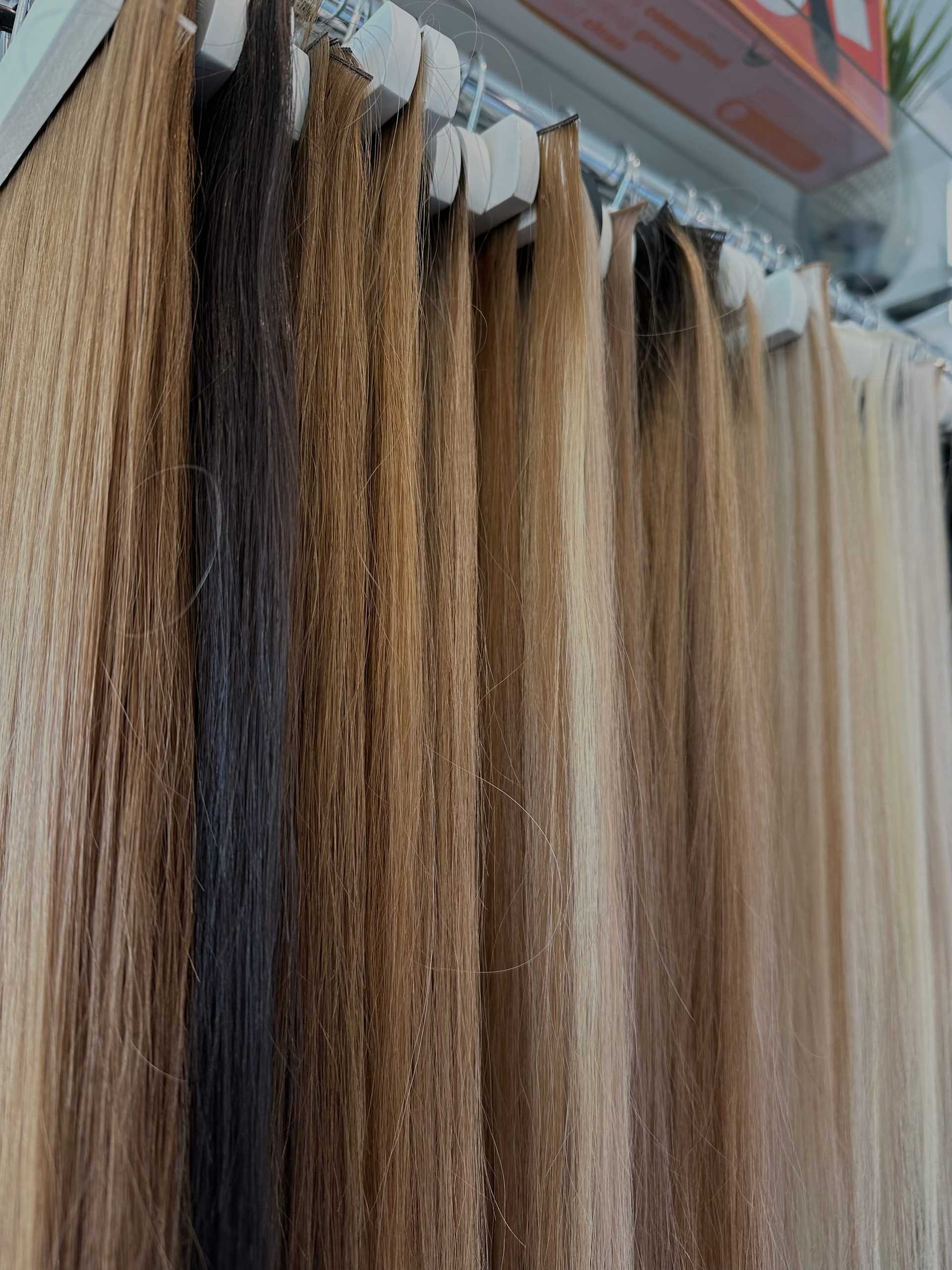 Various shades of hair extensions displayed on hooks in a store setting.