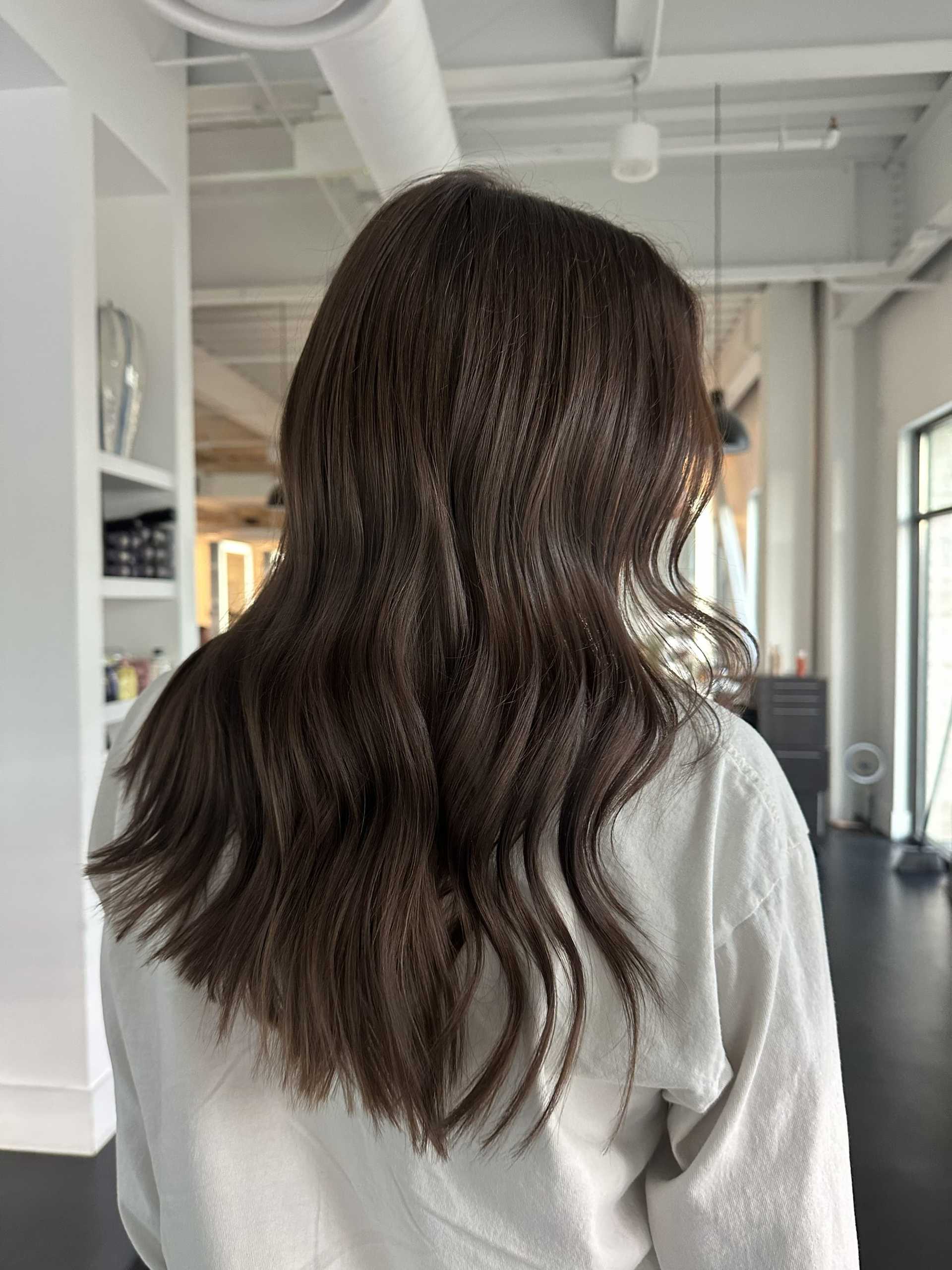 Back view of a person with long wavy brown hair in a modern, well-lit interior space.