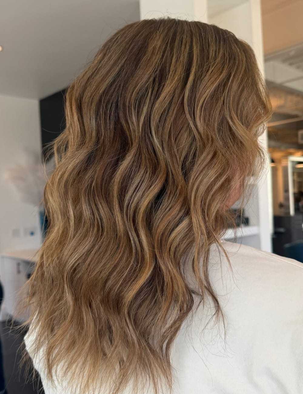 Wavy brown hair with blonde highlights styled in loose curls from a rear view.