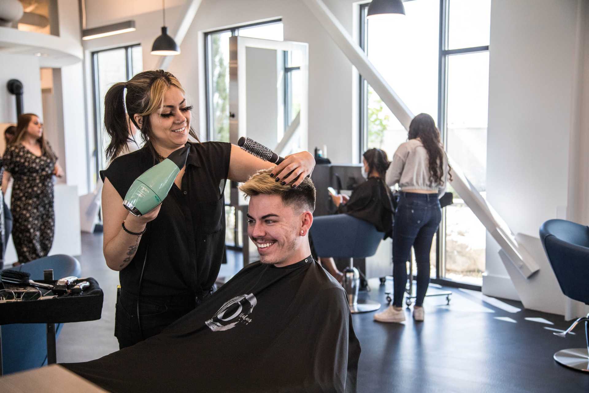 Hairdresser styling a smiling man's hair in a modern salon setting.