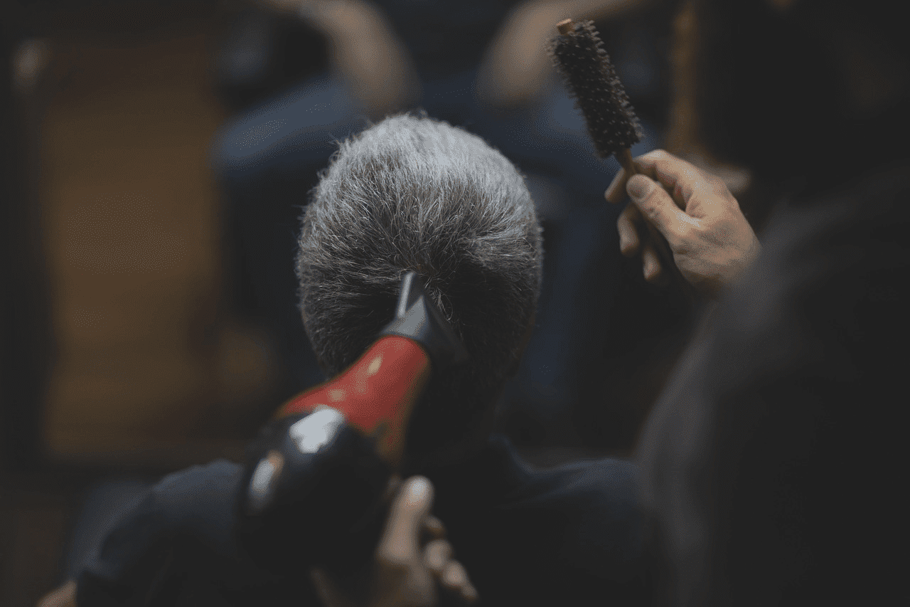 Hairdresser styling a client's hair with a brush and blow dryer in a salon setting.