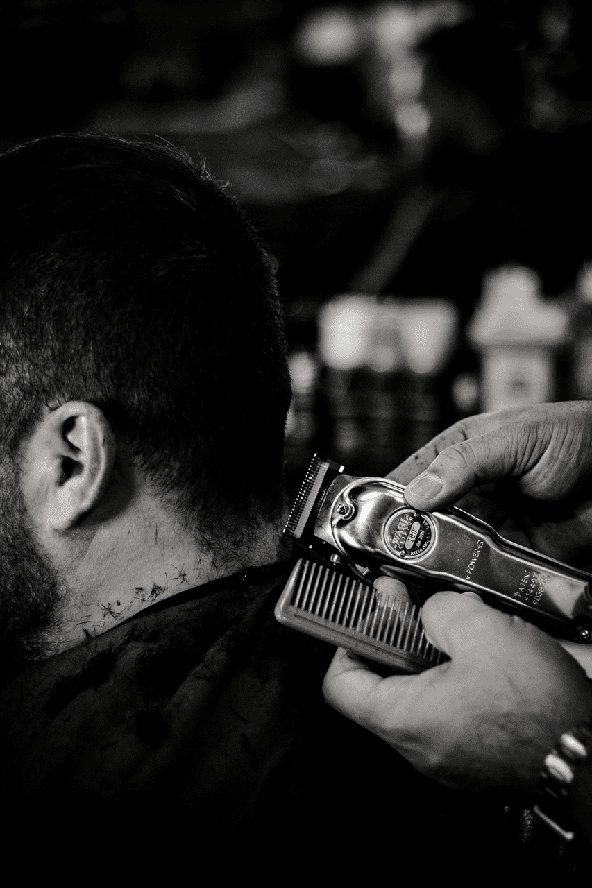 Man getting a haircut with electric clippers, barber trimming the back of his head.