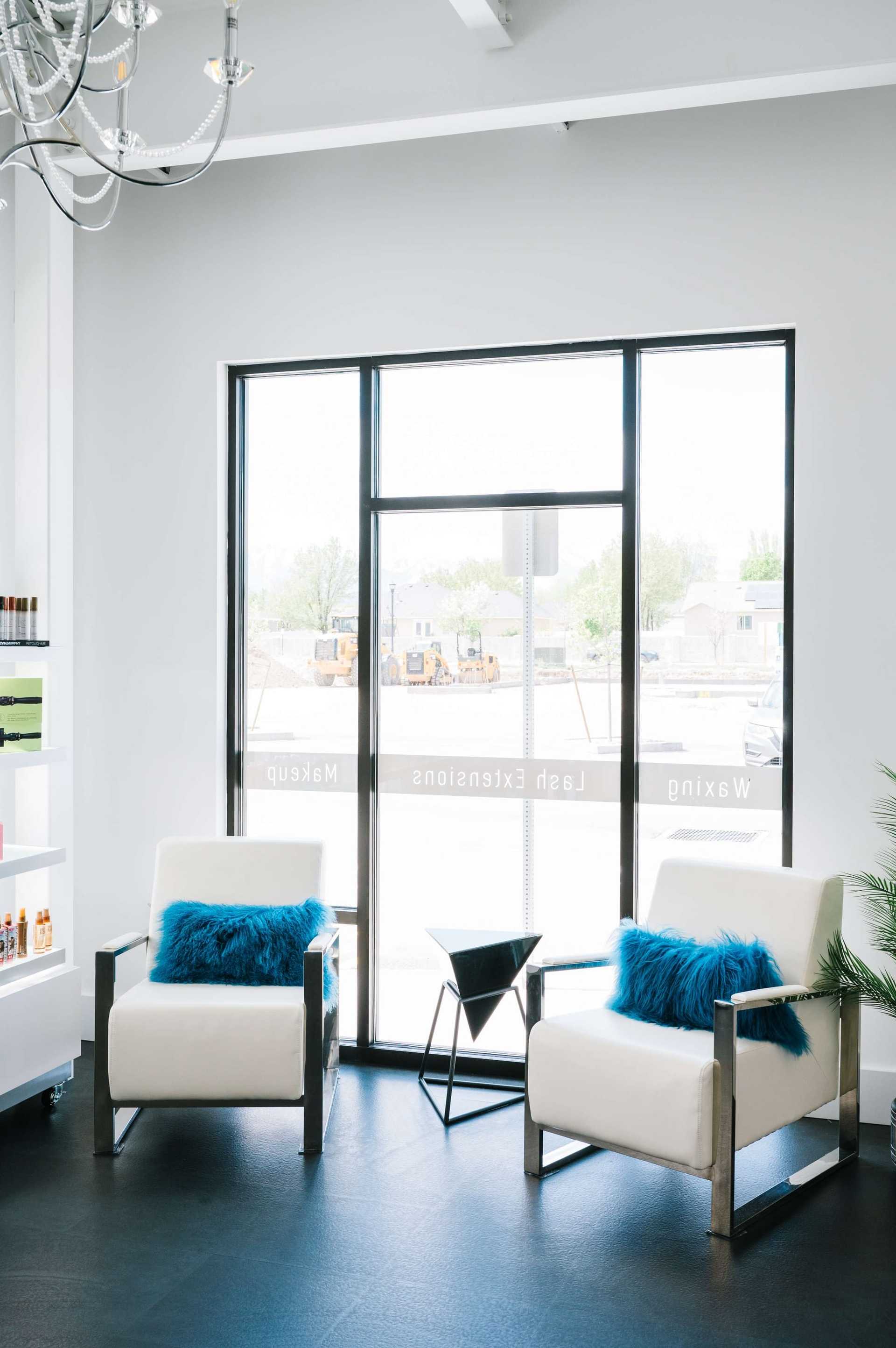 Cozy salon with two white chairs, blue pillows, and a large window displaying natural light.