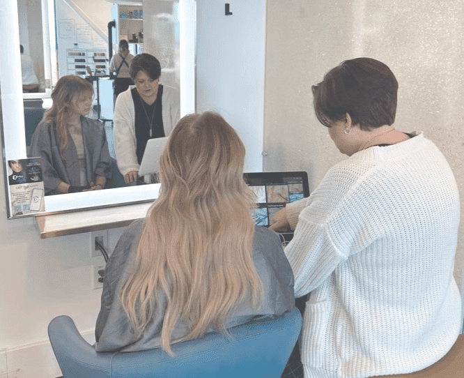 Two people sitting at a salon booth, with one getting a hair consultation.