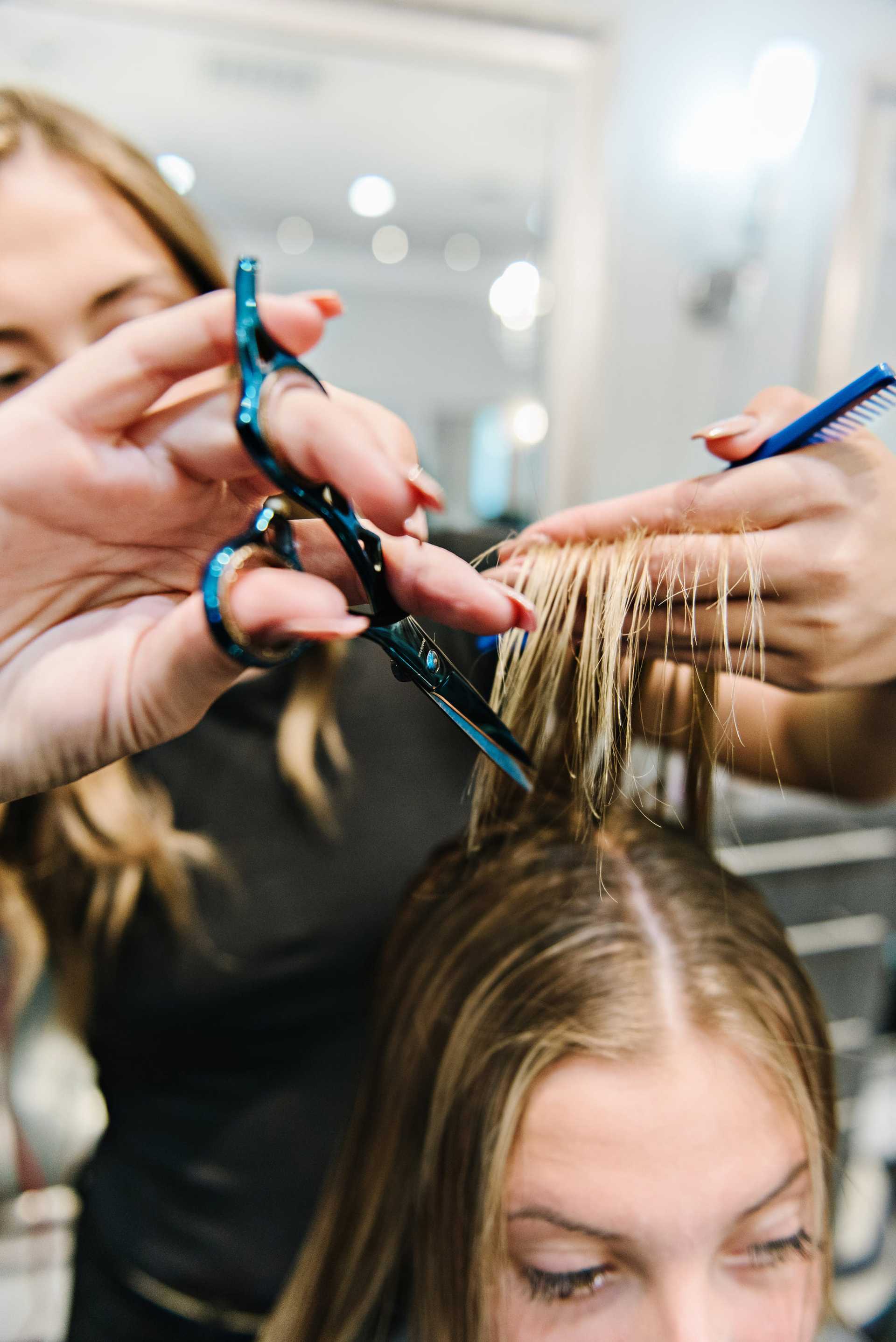 Hairdresser trimming a woman's hair with scissors and comb in a salon setting.