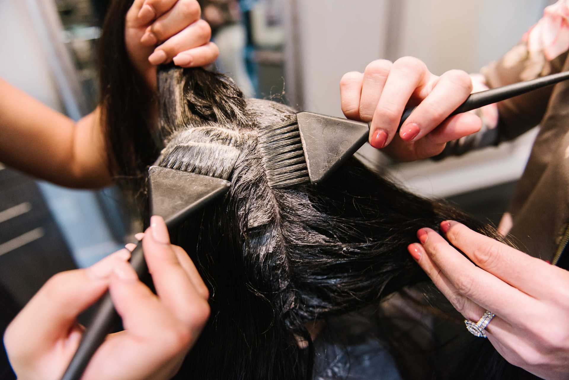 Hairdresser applying dye to woman's hair using brushes and foils.