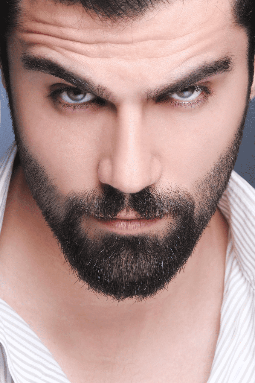 Man with a thick beard and intense gaze, wearing a light-colored shirt.