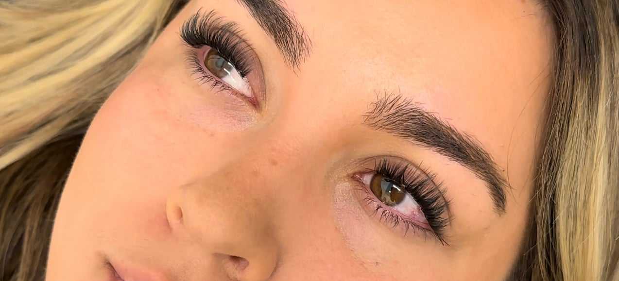 Close-up of a woman's face with full eyebrows and long eyelashes, looking upwards.