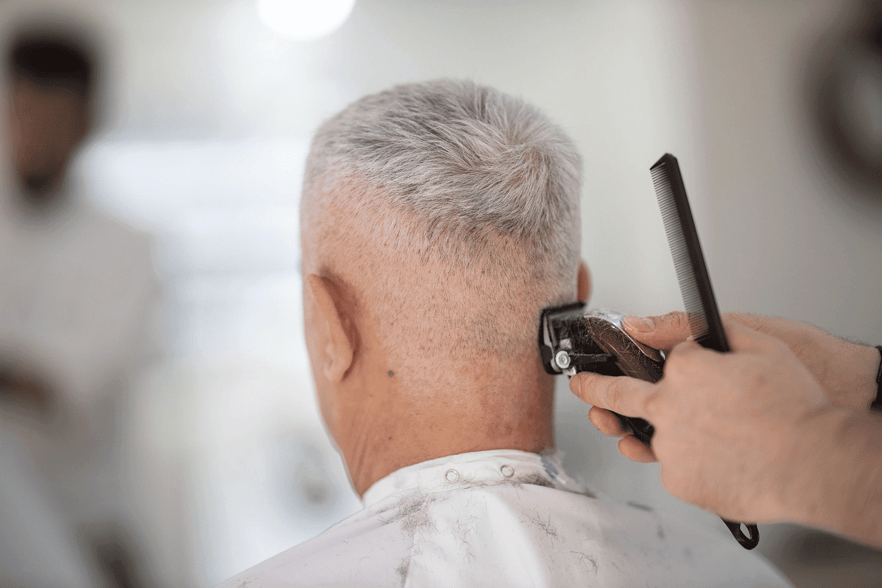 Haircut in progress for a person with short gray hair, using clippers and a comb.