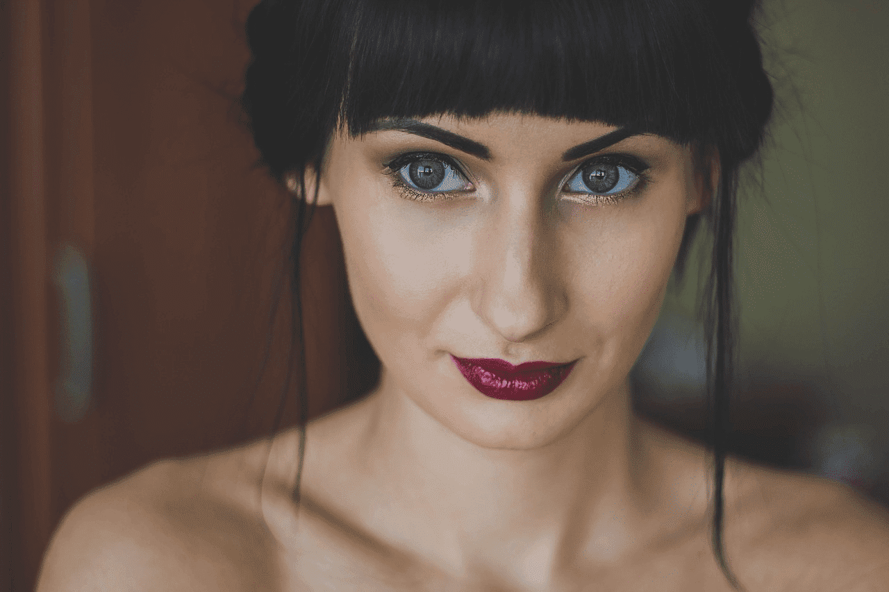 Portrait of a woman with dark hair and makeup, vibrant red lipstick, and piercing eyes.