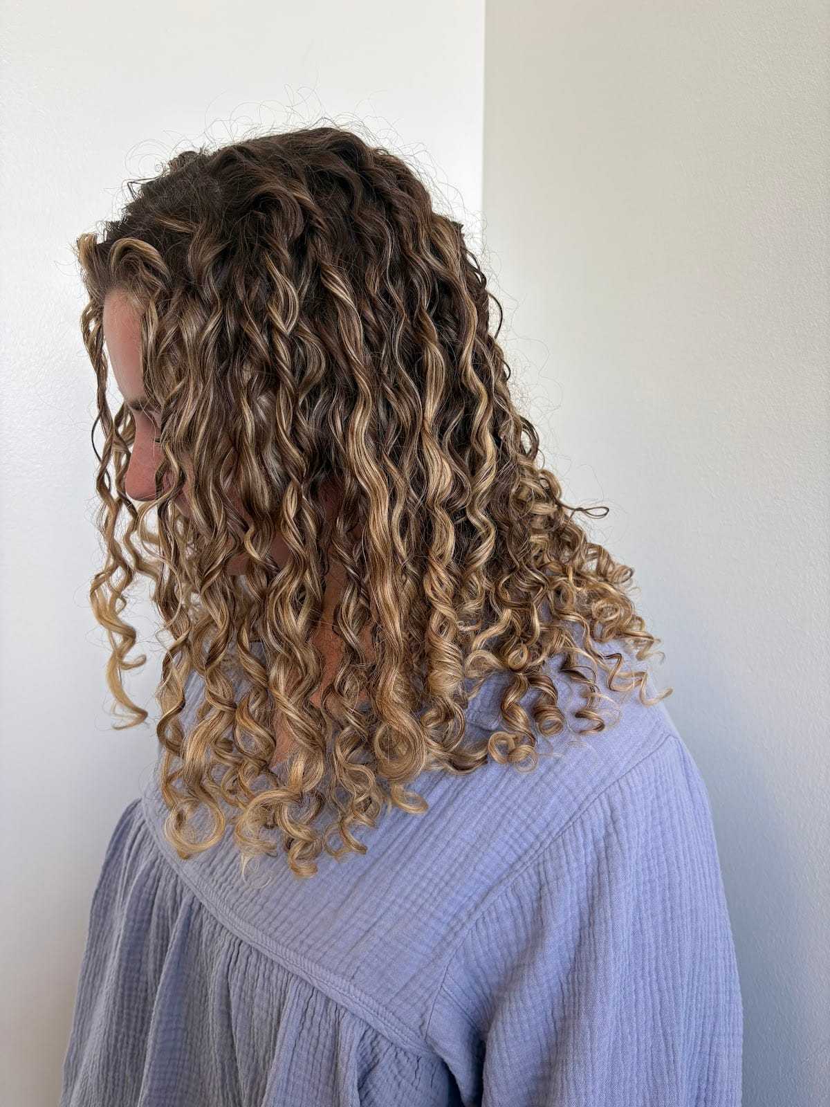 Curly-haired person in a light blue shirt looking down and to the side.