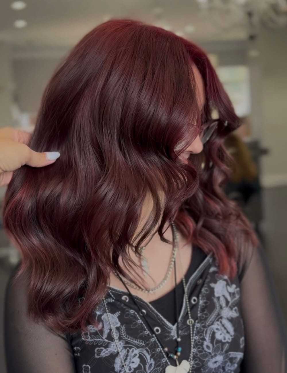 Woman with shoulder-length, wavy burgundy hair in a salon setting.