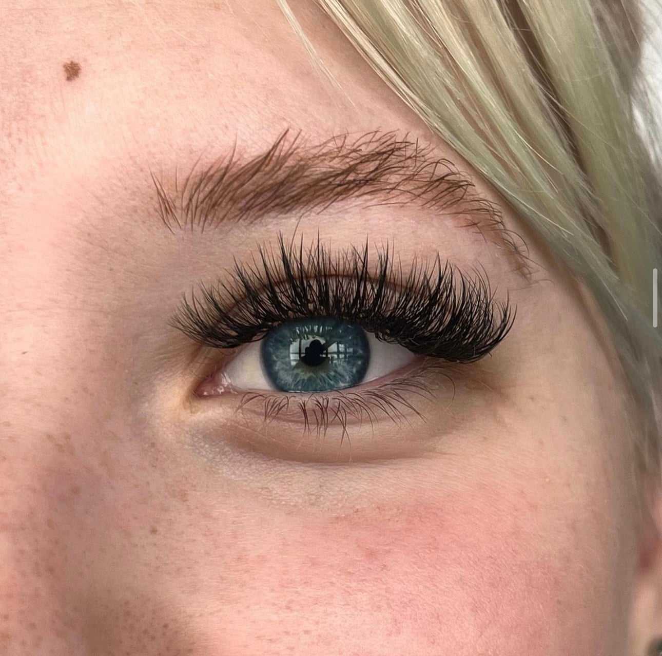 Close-up of a blue eye with long, voluminous eyelashes and light blonde hair visible.